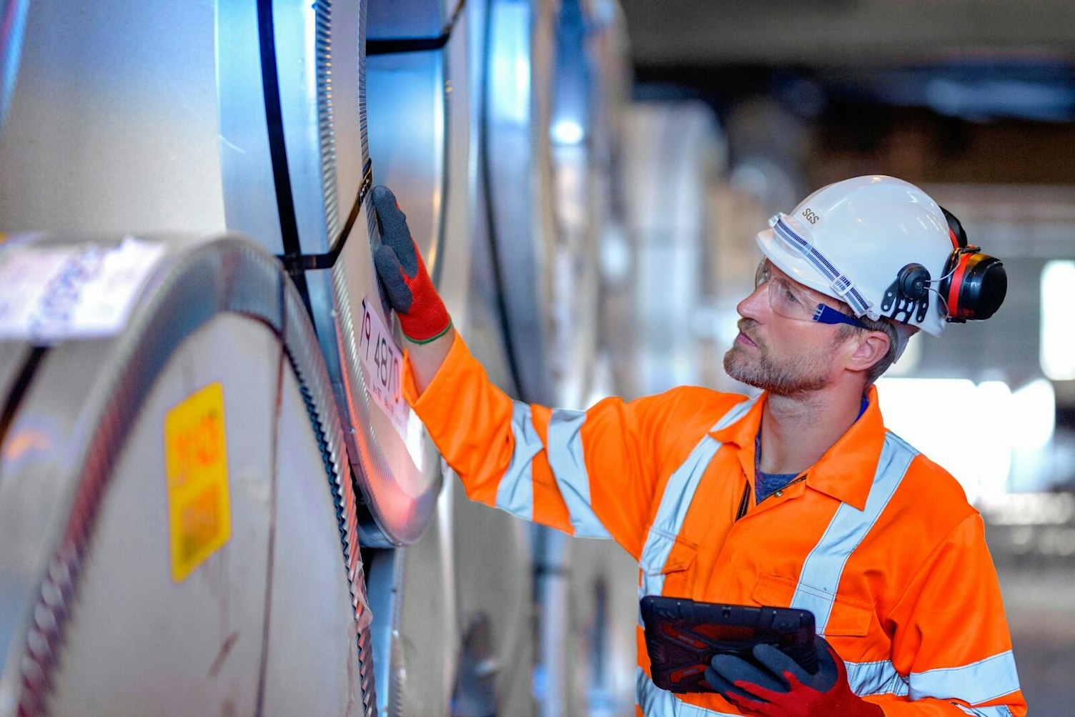 Quality Auditor Using Digital Tablet to Inspect Rows of Sheet Steel