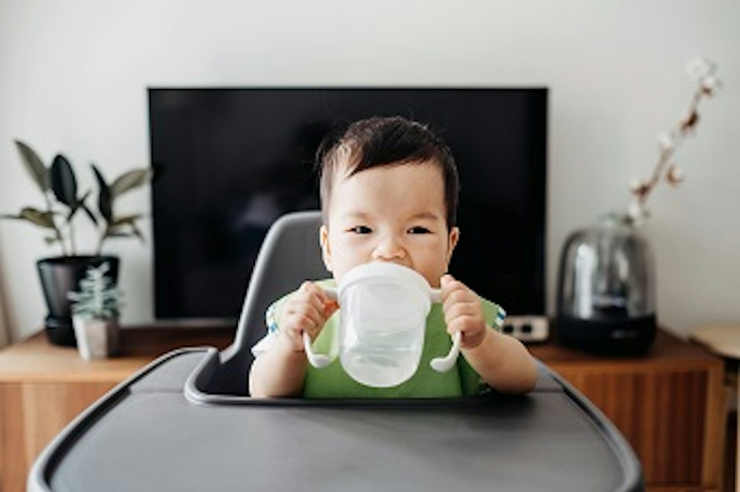 orig cute baby drinking water from sip cup on high chair