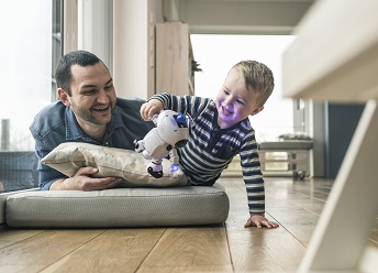 orig excited father and son lying on a mattress at home watching a toy robot