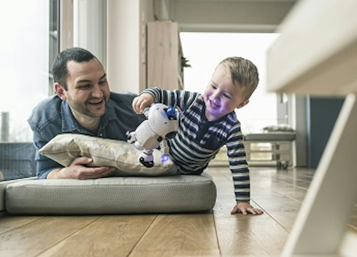 orig excited father and son lying on a mattress at home watching a toy robot