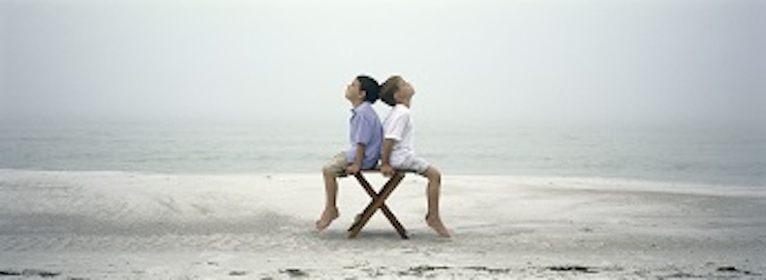 orig two boys sitting back to back on chair on beach