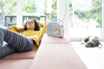 orig woman lying on couch listening to music with portable radio at home