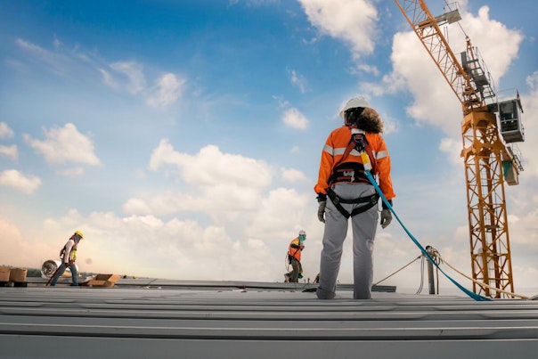 Construction Worker Wearing Safety Harness and Safety Line Working on a Metal Industry Roof