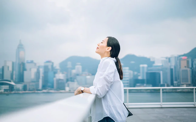 Woman Breathing Fresh Air Against City Background