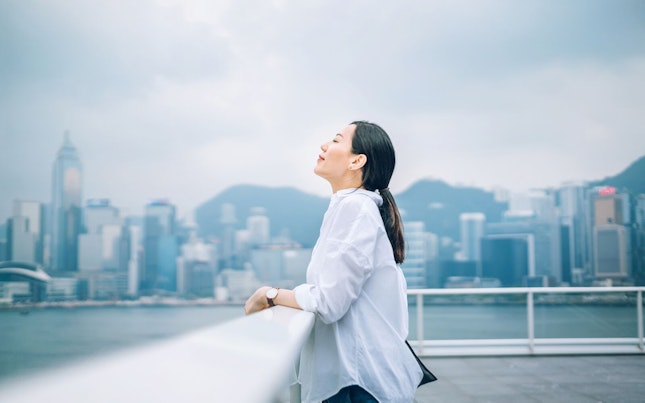 Woman Breathing Fresh Air Against City Background